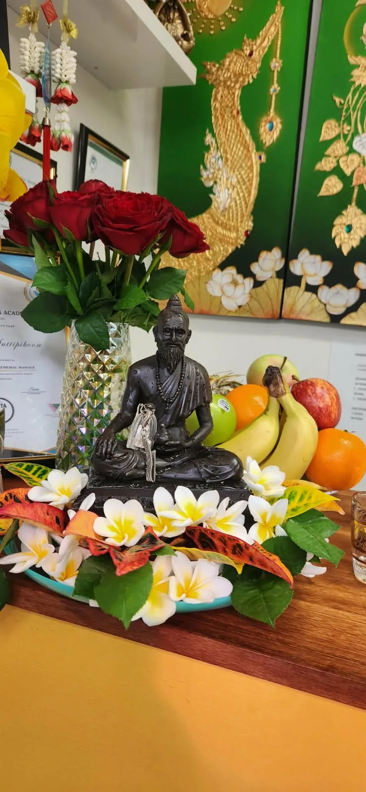 Reusi master statue shrine with red roses, frangipani flowers and fresh fruit offerings